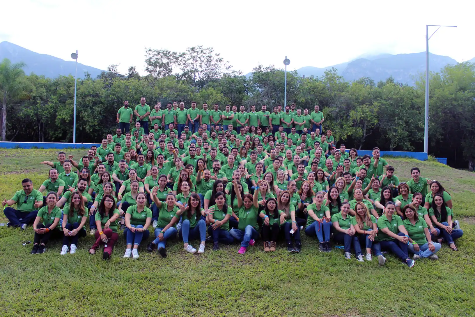 Grupo numeroso de participantes de ALYAX con playeras verdes, reunidos en un jardín frente a las montañas