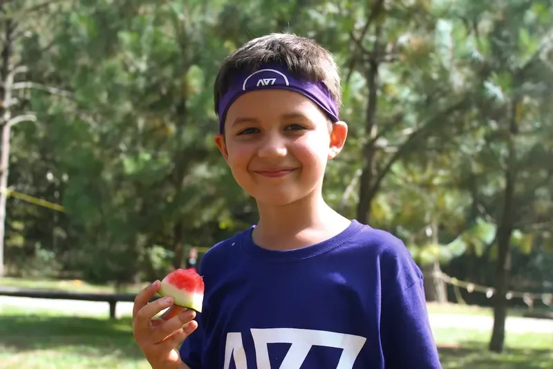Niño con banda morada y playera de ALYAX sonriendo