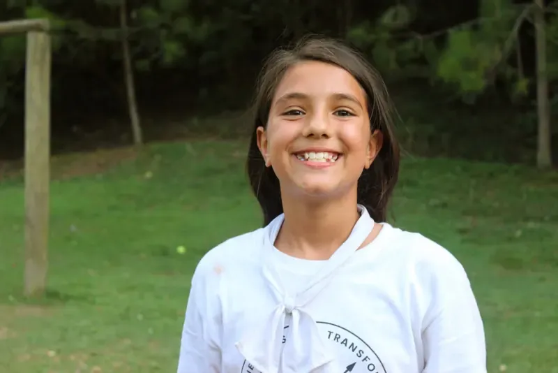 Niña con playera blanca sonriendo en el bosque
