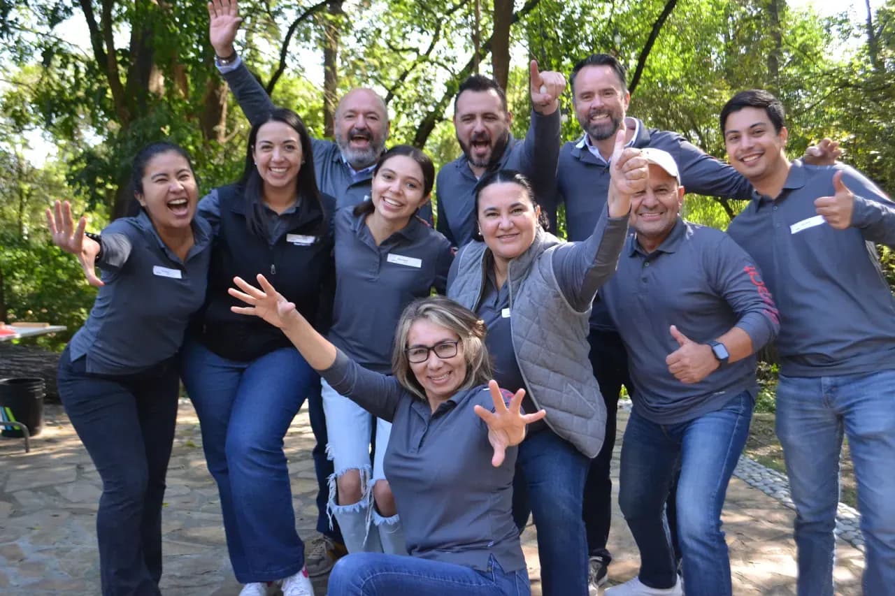 Grupo de colaboradores con playeras grises riendo y posando juntos al terminar una actividad de integración