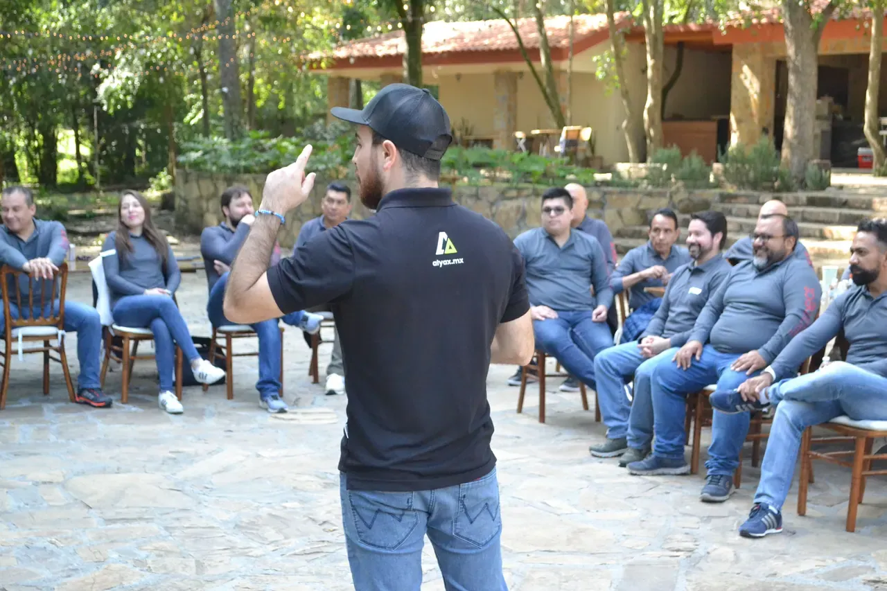Facilitador de ALYAX dando indicaciones a un grupo de colaboradores sentados al aire libre