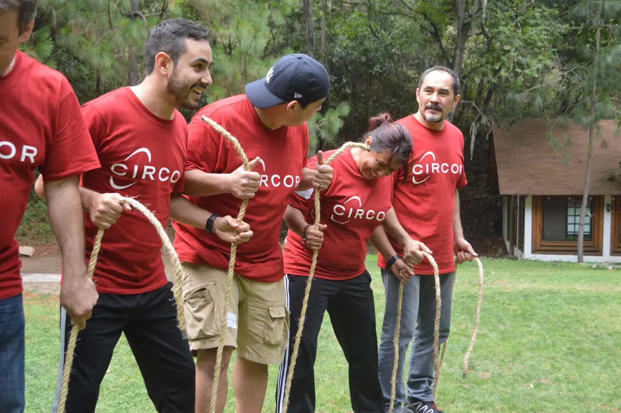 Colaboradores con playeras rojas jalando cuerdas en una actividad de integración en el bosque
