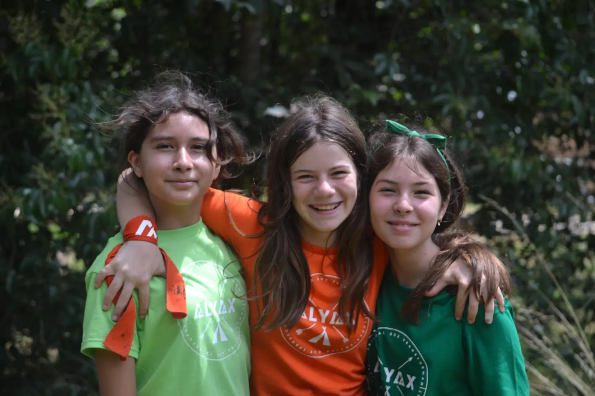 Tres niñas sonrientes abrazadas en el campamento