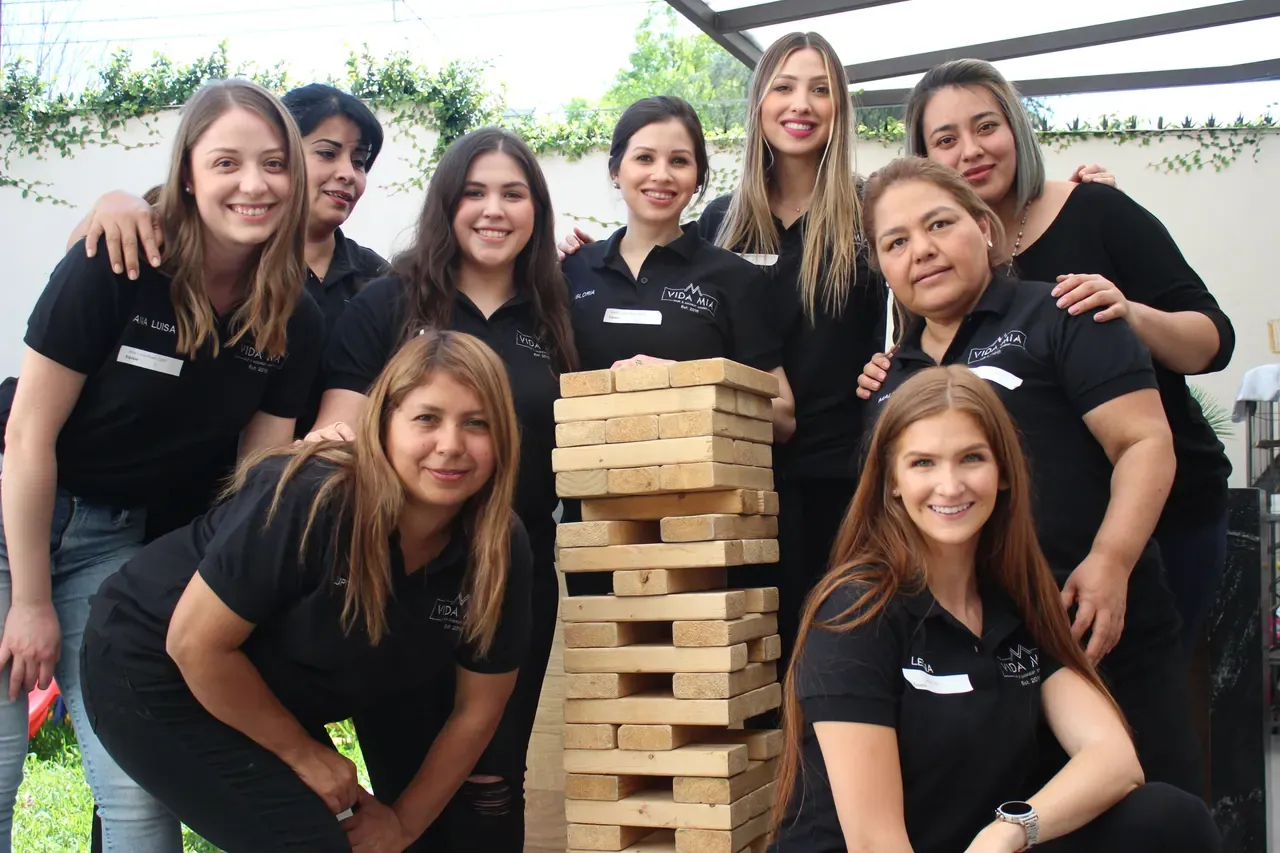 Colaboradoras sonrientes alrededor de una torre de bloques de madera en un curso de trabajo en equipo