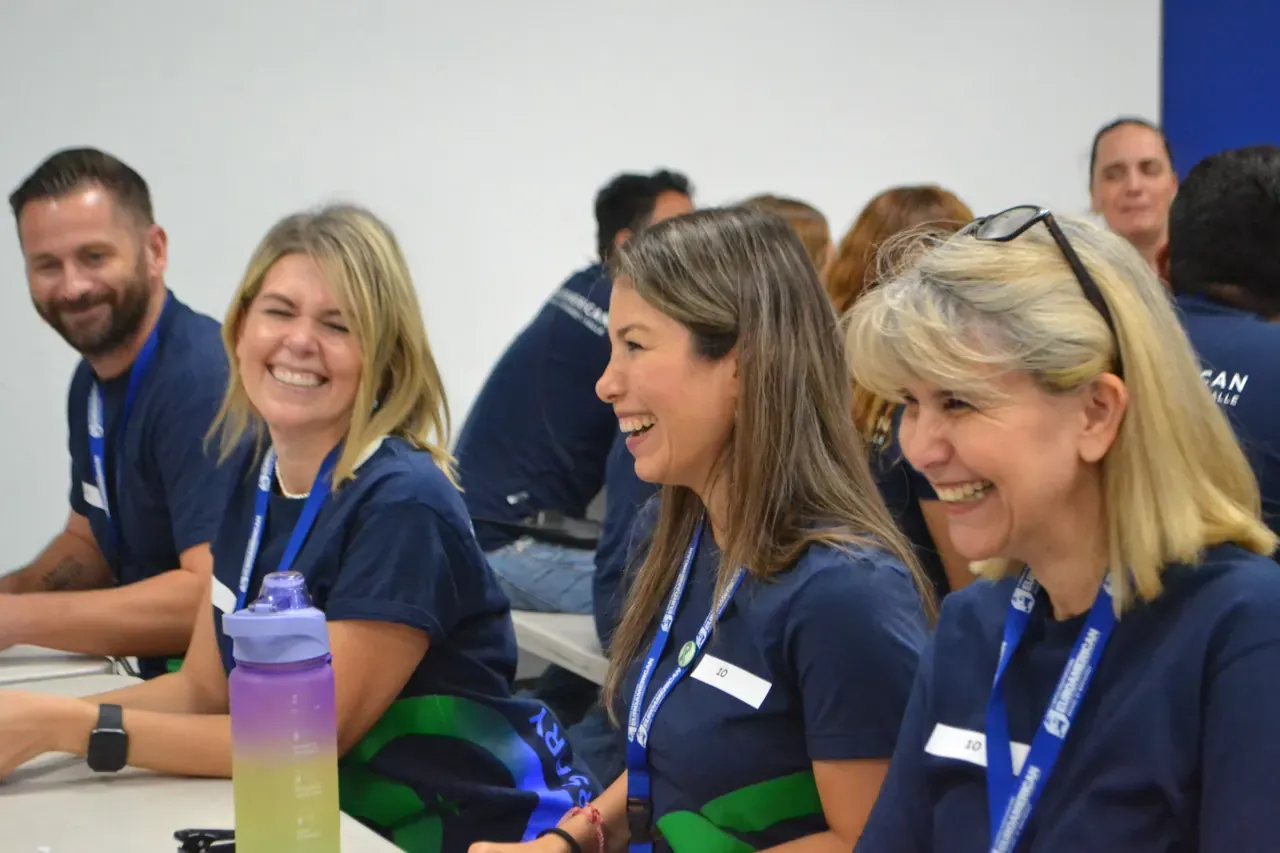 Maestra compartiendo una sonrisa con sus compañeros mientras completan una actividad de integración
