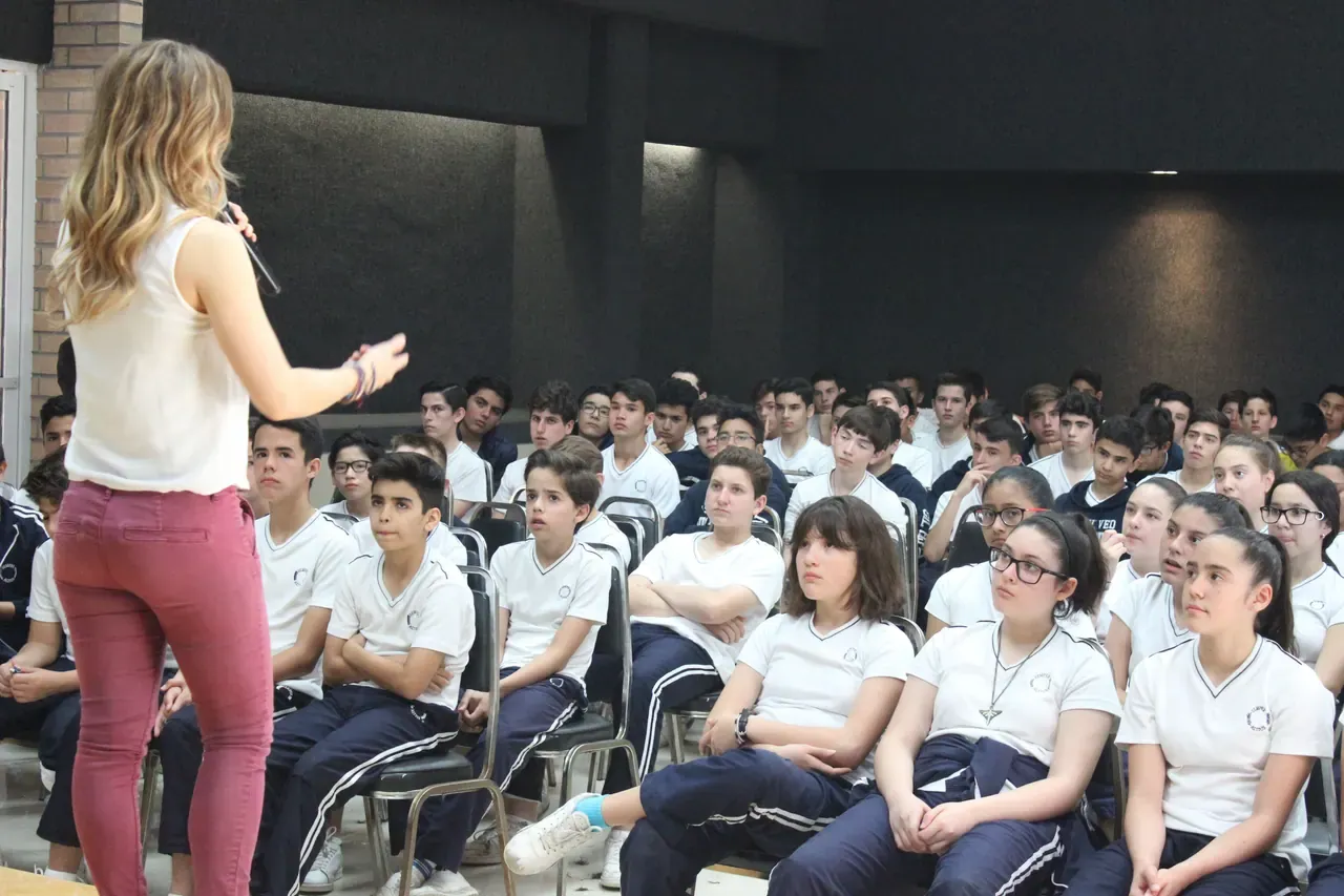 Ponente hablando frente a un grupo grande, destacando la conexión entre motivación y resultados positivos