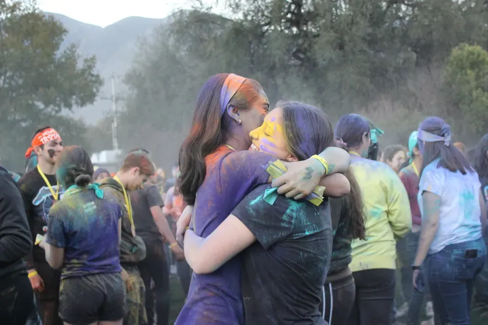 Dos campistas abrazadas al terminar una actividad, cubiertas de polvos de colores
