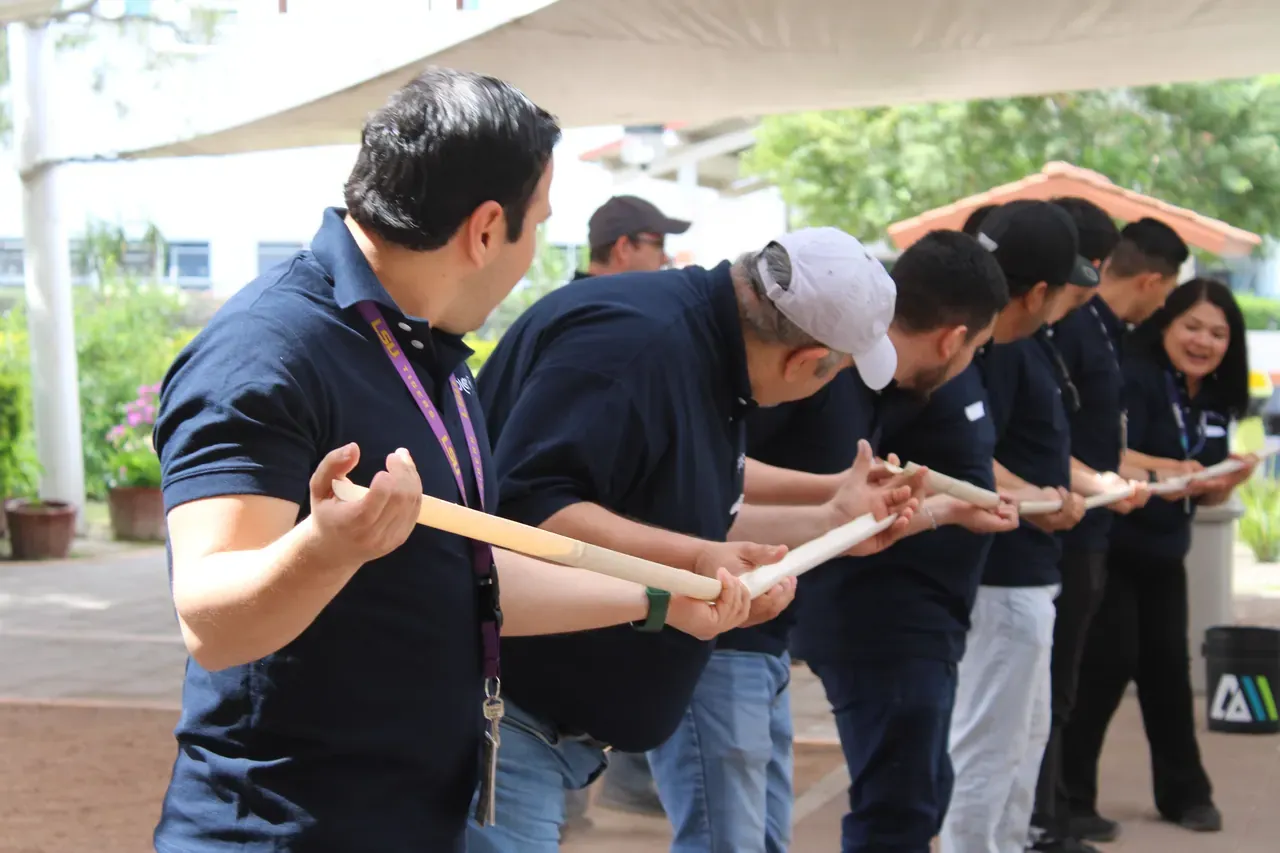 Equipo de colaboradores coordinándose para sostener varas de madera en fila durante una dinámica