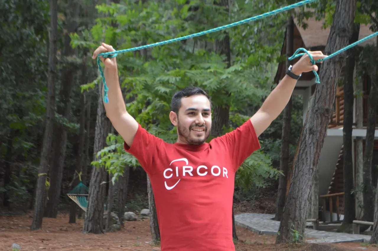 Colaborador sonriente con los brazos en alto sosteniendo una cuerda en un reto al aire libre
